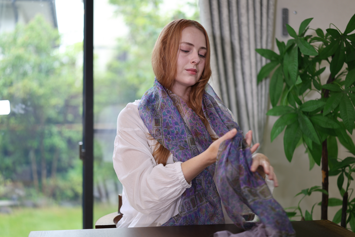 Model seated at a table guiding one end of the purple double-woven Edo Sarasa silk stole through her hands.