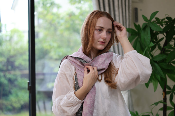A model wearing the pale purple side of the reversible sumo-pattern silk stole beside a table and bright window.