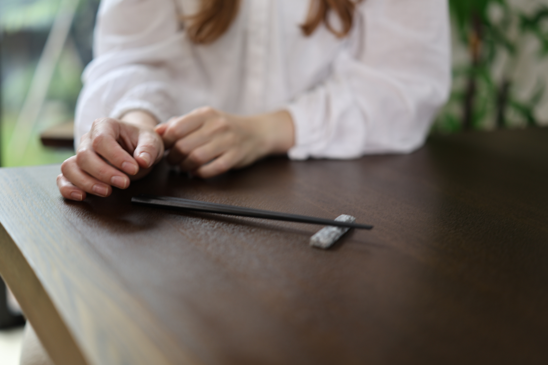 An adult arranging black chopsticks beside a Makabe stone cutlery rest on a dark wooden table.