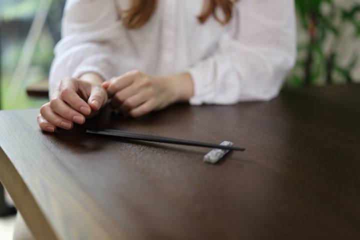 An adult arranging black chopsticks beside a Makabe stone cutlery rest on a dark wooden table.