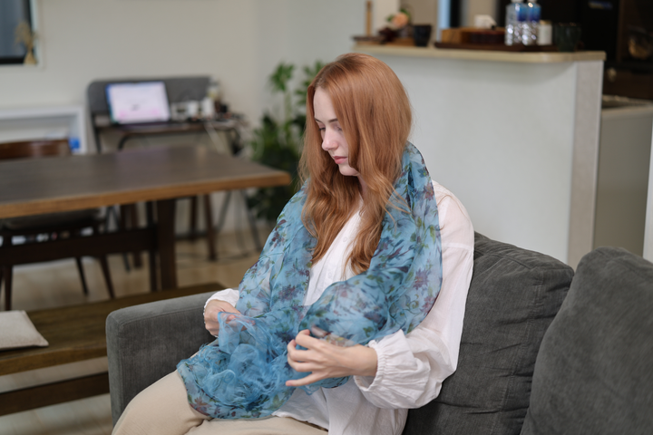 A seated model wearing the blue silk stole spread across the torso and lap on a grey sofa.