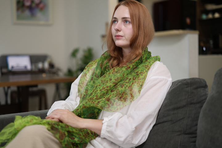A seated model wearing the green Edo Sarasa silk stole broadly draped across her shoulders and lap.