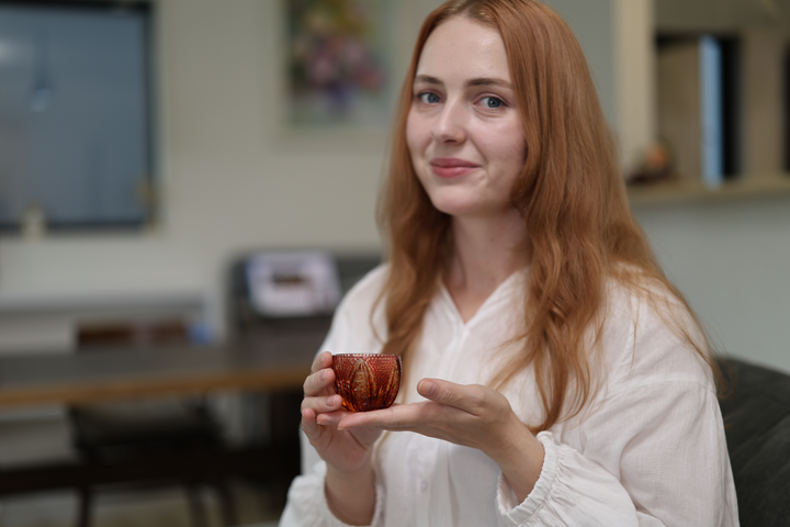 Adult model seated on a sofa presenting the GENEN Gold-Red and Amber Edo Kiriko glass between both hands.