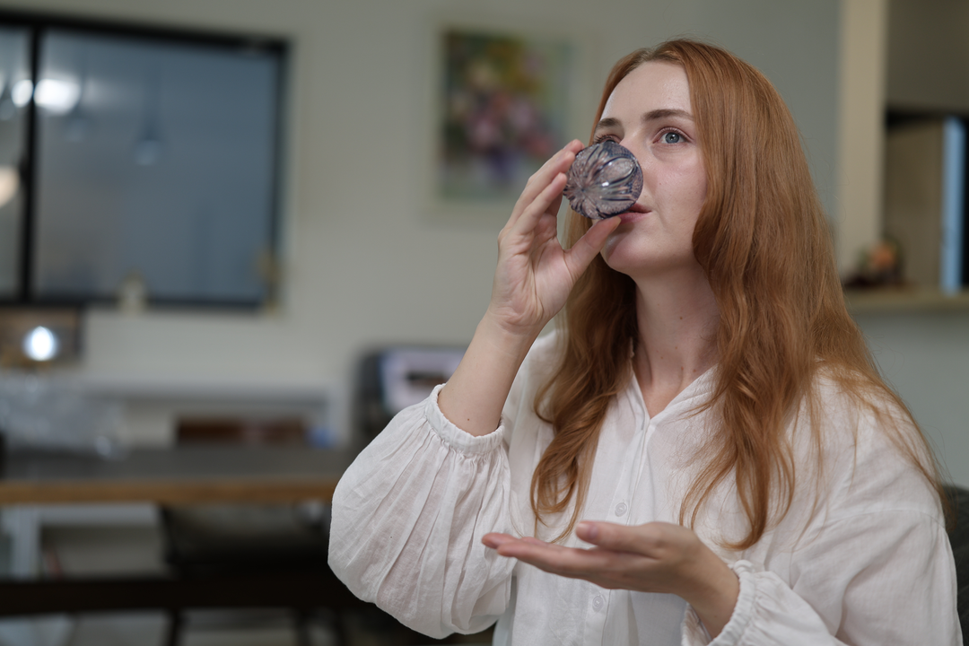 A seated model drinking from the GENEN Indigo cut-glass vessel in a relaxed interior.