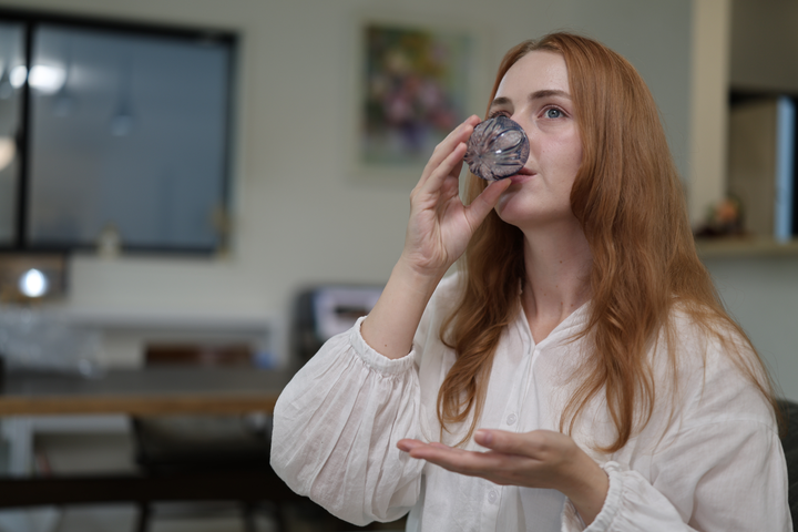A seated model drinking from the GENEN Indigo cut-glass vessel in a relaxed interior.