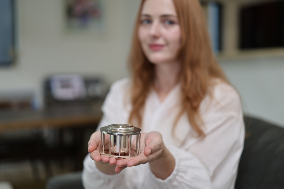 A seated model presenting the pure silver incense burner on open palms from a sofa.