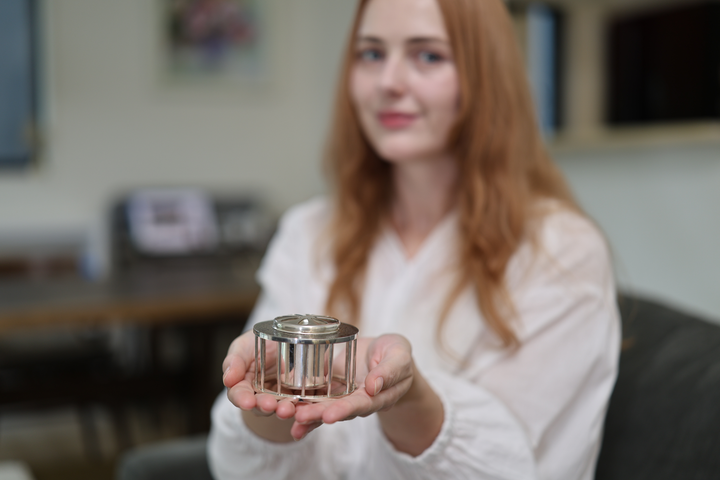 A seated model presenting the pure silver incense burner on open palms from a sofa.