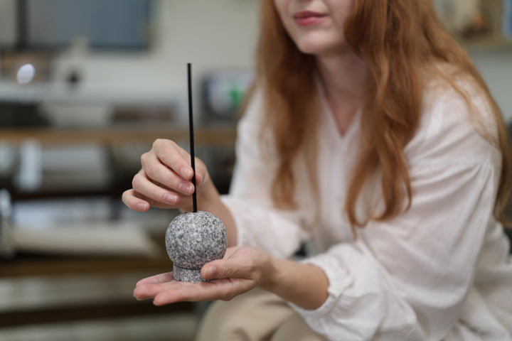 A seated model holding the cool Makabe Stone Incense Stone in one palm beside a sofa before use.