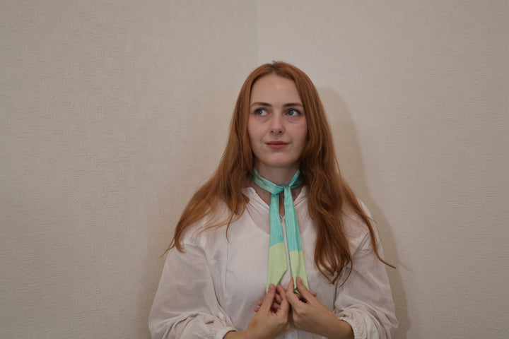 A model holding the tapered ends of the green silk scarf beneath a small neck knot in a quiet Japanese room.