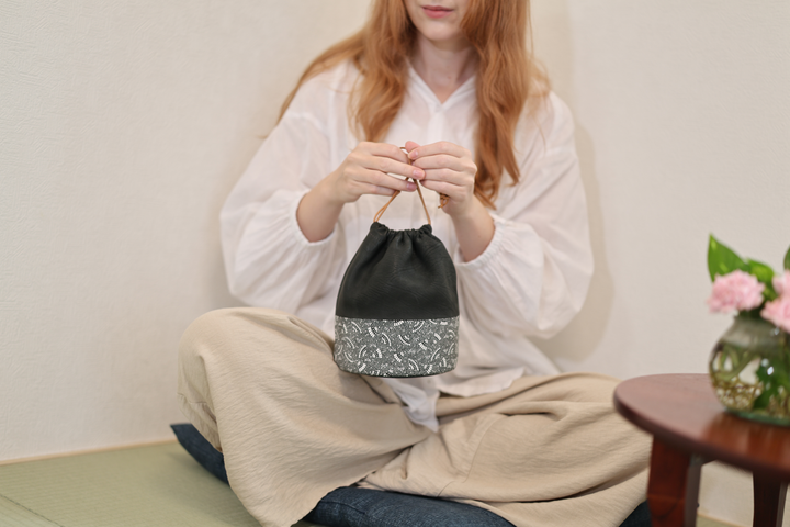 Seated adult model holding the black Edo Komon drawstring pouch with both hands in a tatami room.