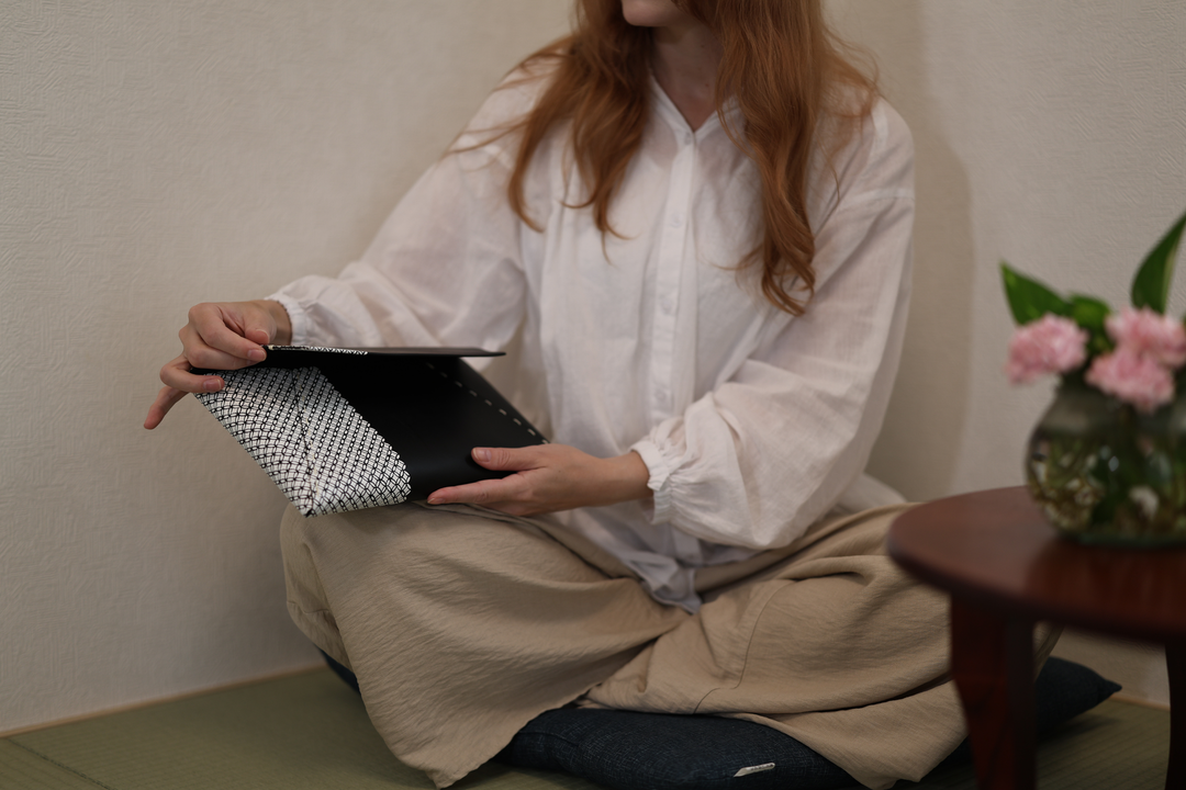 A seated model opening the black-and-white Tokyo Some-Komon clutch in a tatami room.