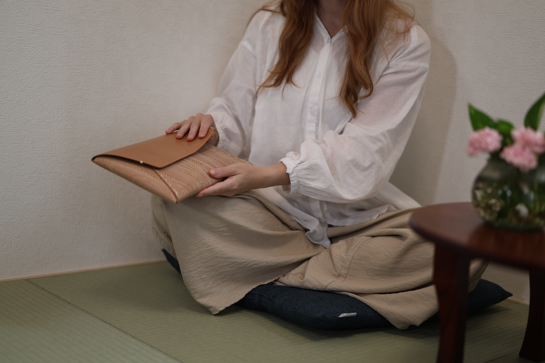 A seated model guiding the natural leather Tokyo Some-Komon clutch closed in a tatami room.