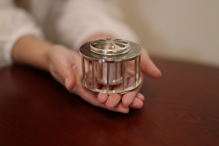 A model cupping the assembled pure silver incense burner in both hands above a low wooden table.
