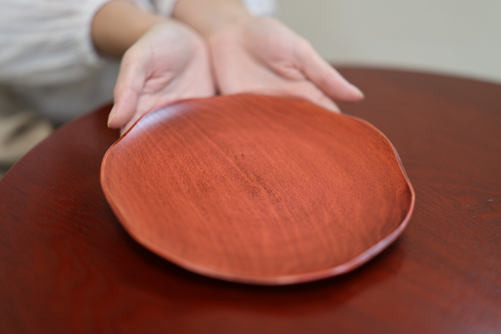 Open hands presenting the berry-red RIN 7.0 plate on a red lacquered table.