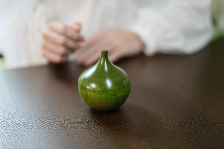 Closed Bulb: Olive on a dark wood table with a person's hands softly out of focus in the background.
