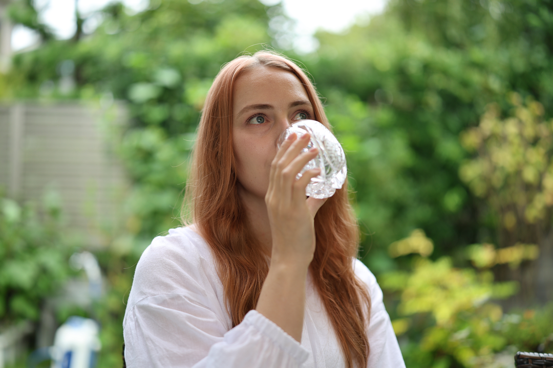 An adult taking a sip from SHIROHANA: Clear in a green garden setting.