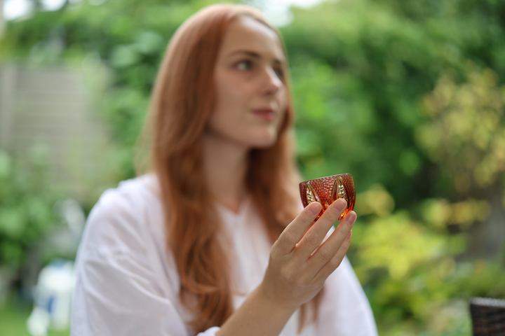 Adult model holding the GENEN Gold-Red and Amber Edo Kiriko glass at chest height in a garden.