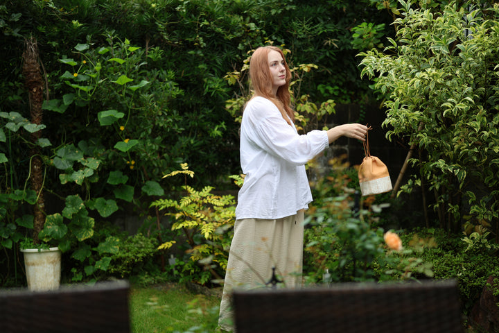 A model carrying the natural leather Edo Komon drawstring pouch at her side in a green garden.