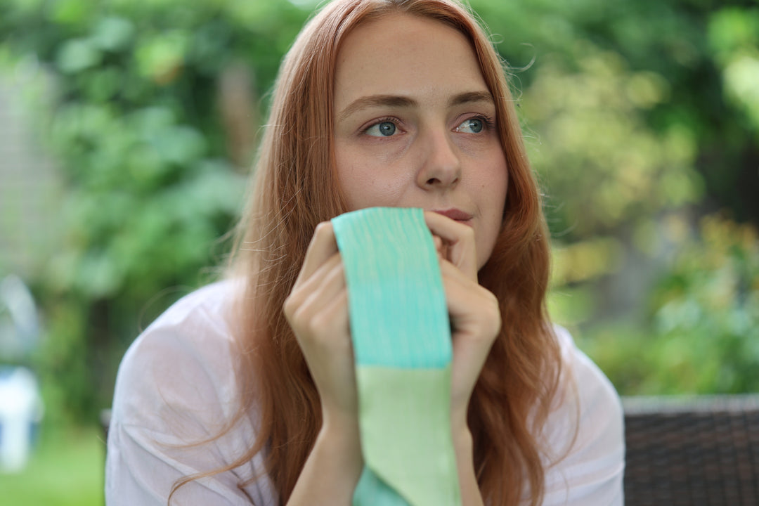 A model holding the green bamboo-pattern silk scarf close to her face against a soft garden background.