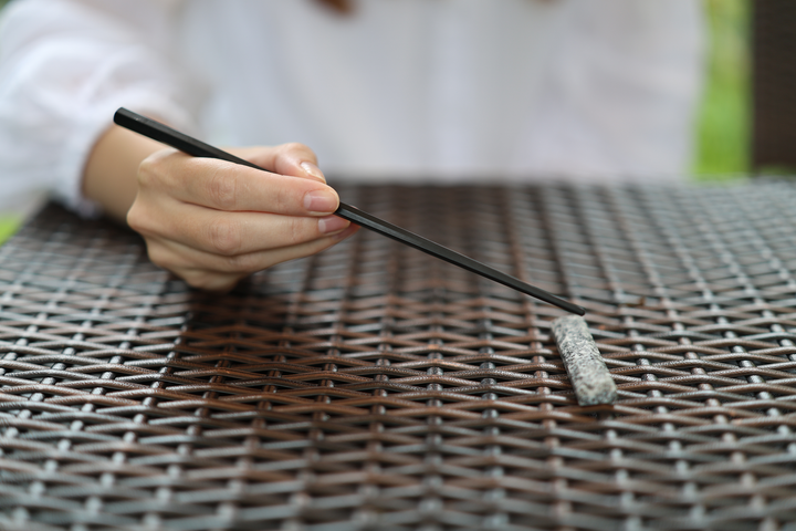 An adult holding black chopsticks above a Makabe stone cutlery rest on a dry woven outdoor table.