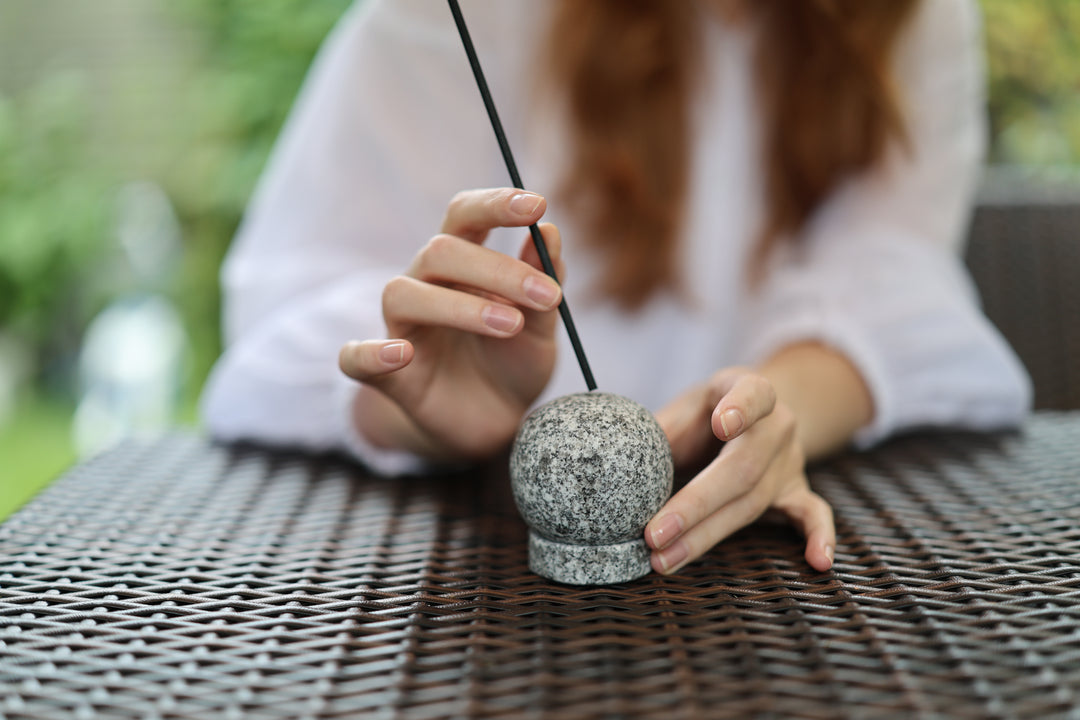 A model setting an unlit incense stick in the Makabe Stone Incense Stone on a stable outdoor table.