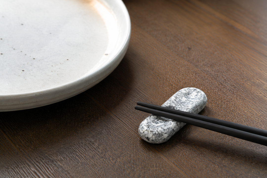 Makabe stone cutlery rest holding black chopsticks beside a plate on a quiet dining table.