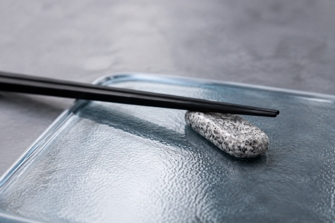 Makabe stone cutlery rest and black chopsticks on a cool textured glass tray.