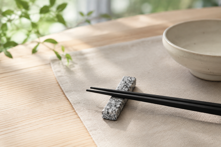 A single Makabe stone cutlery rest holding black chopsticks beside a simple bowl on a calm everyday table.