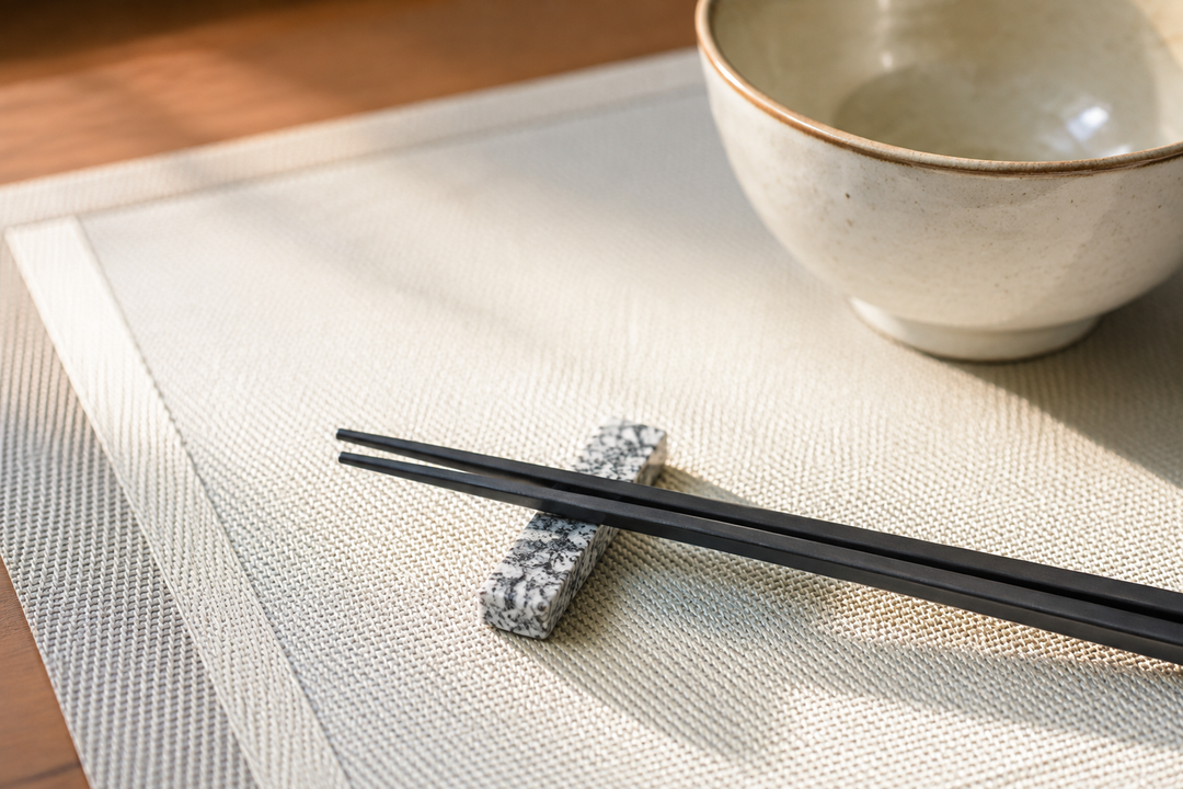 Morning light across a single Makabe stone cutlery rest aligned with a pale breakfast placemat and black chopsticks.