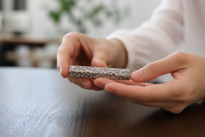 Dry adult hands gently supporting a single Makabe stone cutlery rest for a close look at its top and side grain.