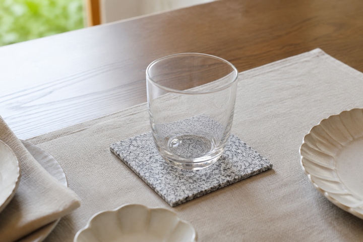 One guest place set with a clear glass on the square Makabe Stone Art Plate at a restrained dining table.