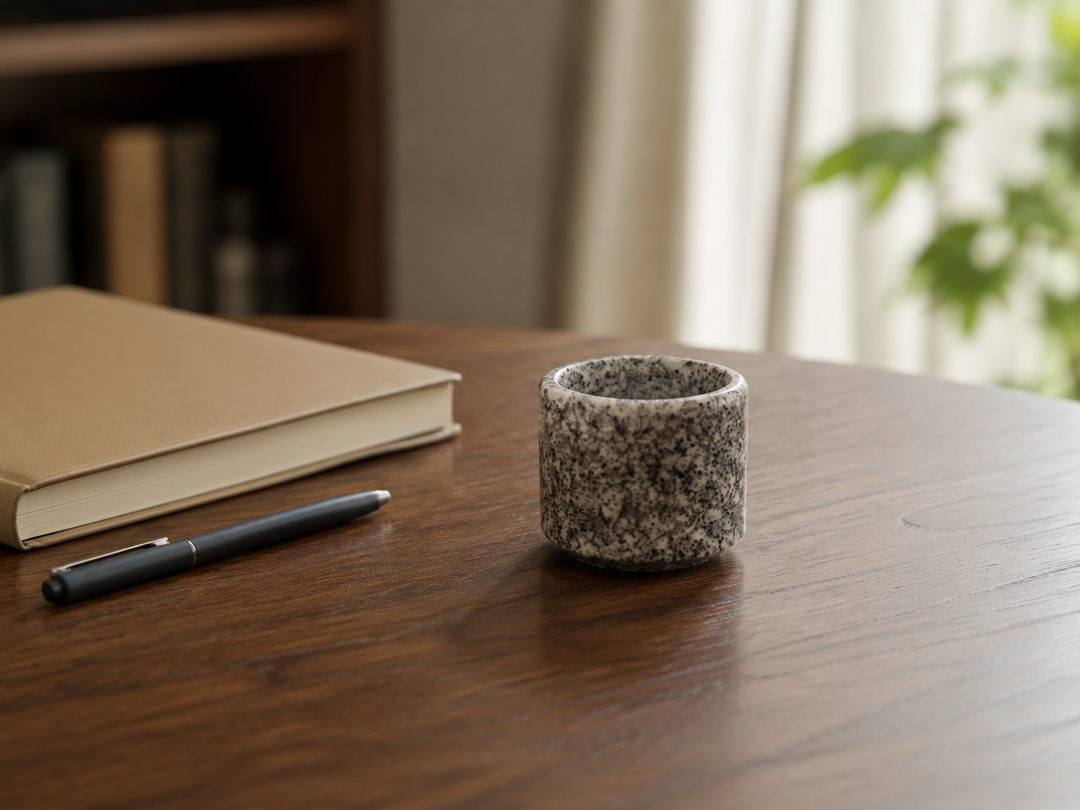 Makabe stone cup alone on a pale wooden table in soft morning window light.