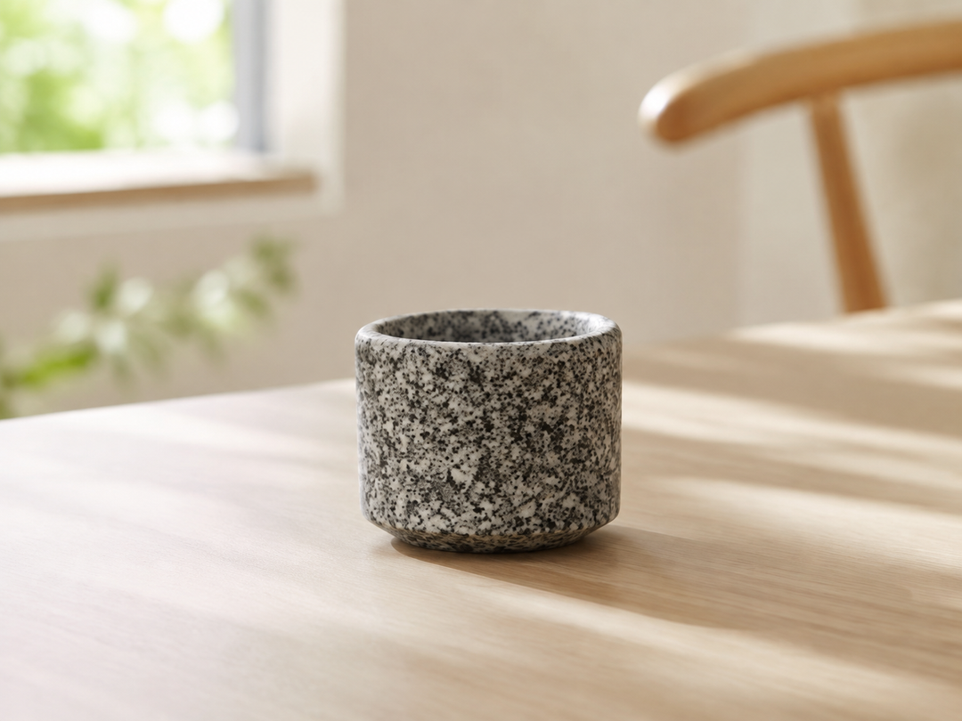 Makabe stone cup beside a closed notebook and pen on a calm wooden desk.