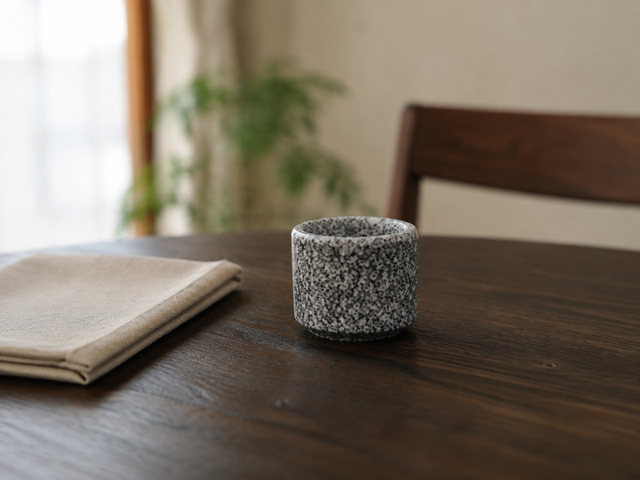 Makabe stone cup as the focal point of a restrained setting with plain linen on a dark wooden table.