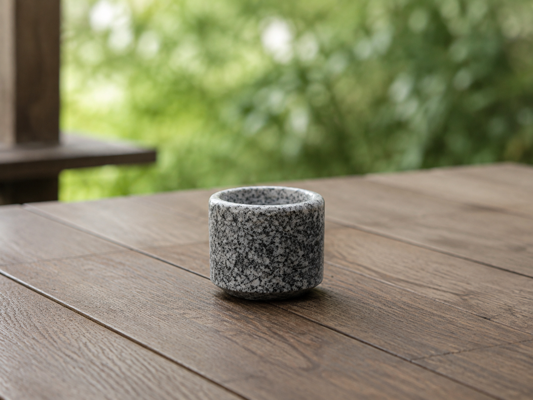 Makabe stone cup on a dry sheltered terrace table with soft greenery in the background.
