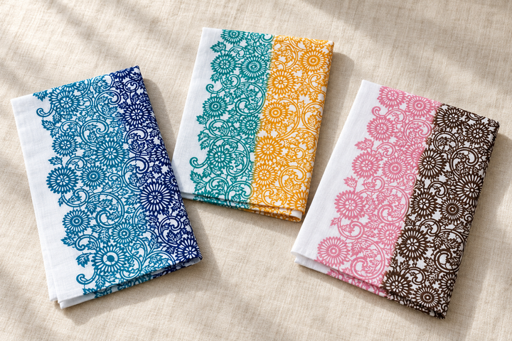 The three Ise-giku tenugui arranged separately on pale fabric, showing their different paired colors and shared floral pattern.
