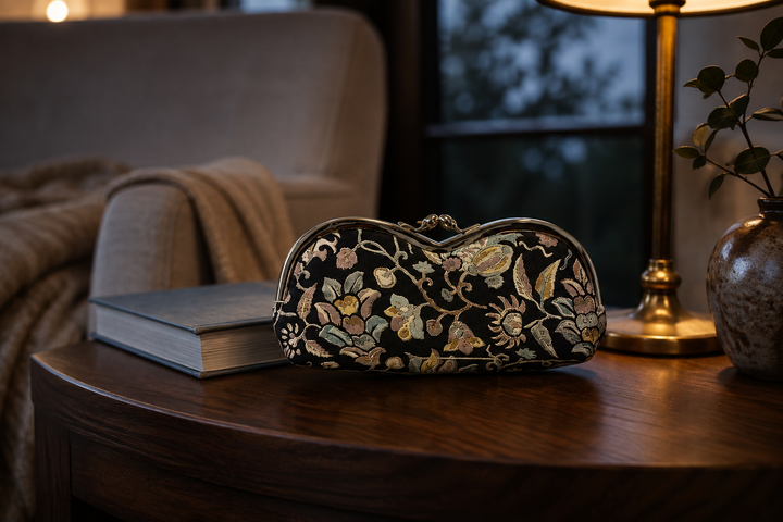 Black Edo Sarasa floral arabesque eyeglass case beside a closed book on an indoor reading table.