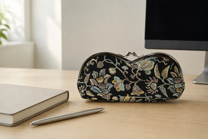 Black Edo Sarasa floral arabesque eyeglass case beside a notebook on an orderly indoor work desk.