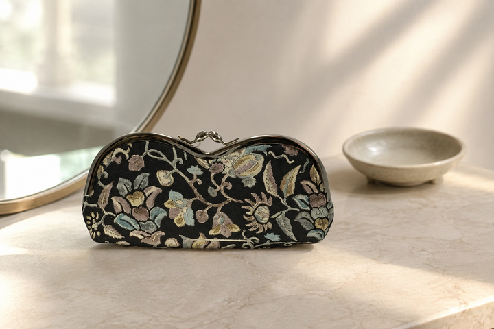 Black Edo Sarasa floral arabesque eyeglass case on a dressing table in soft morning light.