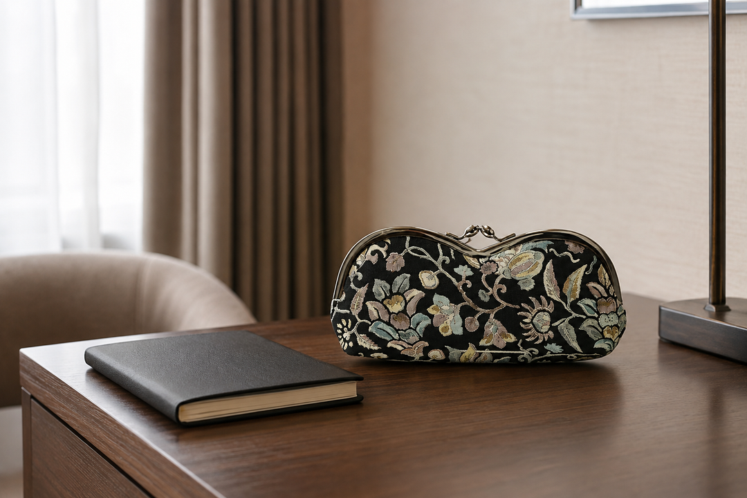 Black Edo Sarasa floral arabesque eyeglass case on a calm hotel-room desk.