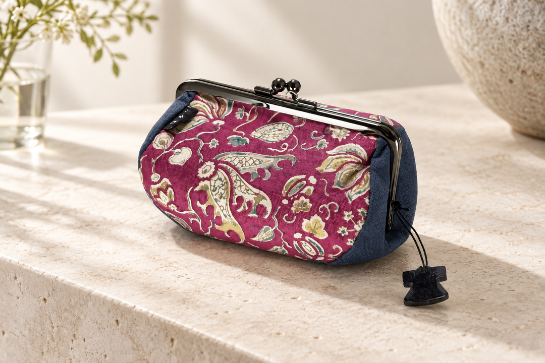 The red and navy floral arabesque pouch standing on pale stone with its metal clasp and silk texture visible.