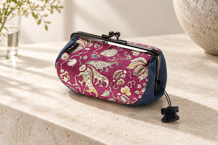 The red and navy floral arabesque pouch standing on pale stone with its metal clasp and silk texture visible.