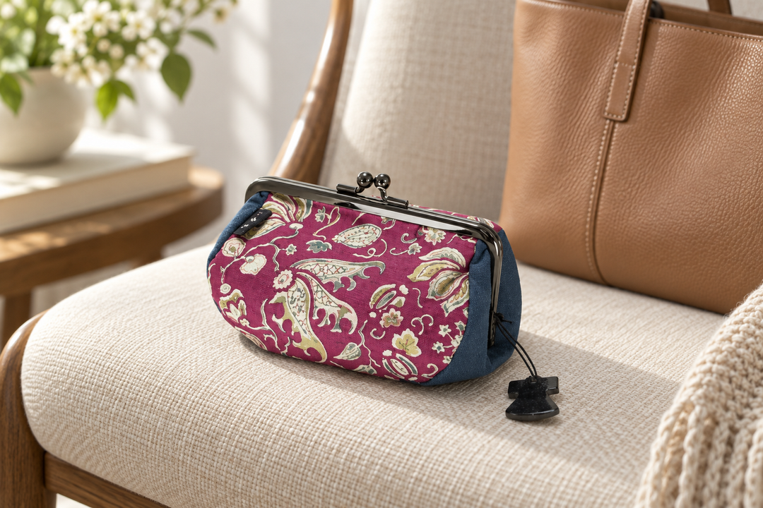 The floral arabesque pouch on a cream upholstered chair in front of a tan leather handbag.