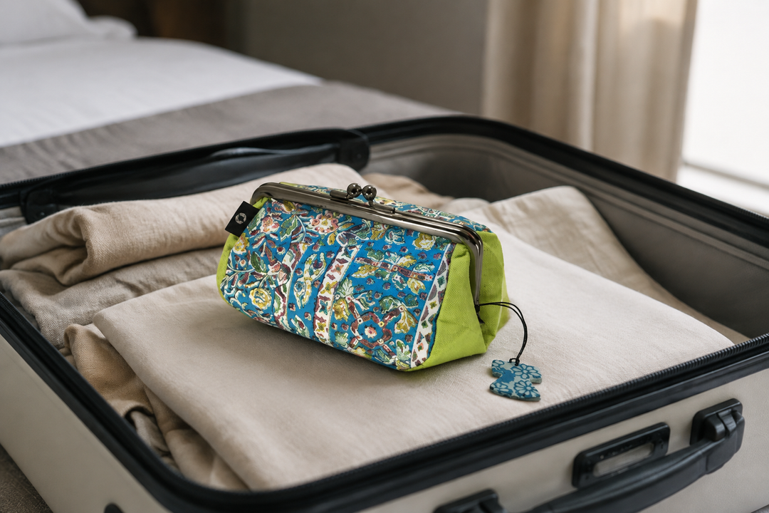 Turquoise and yellow-green Edo Sarasa pouch resting visibly on folded clothing inside an open suitcase.