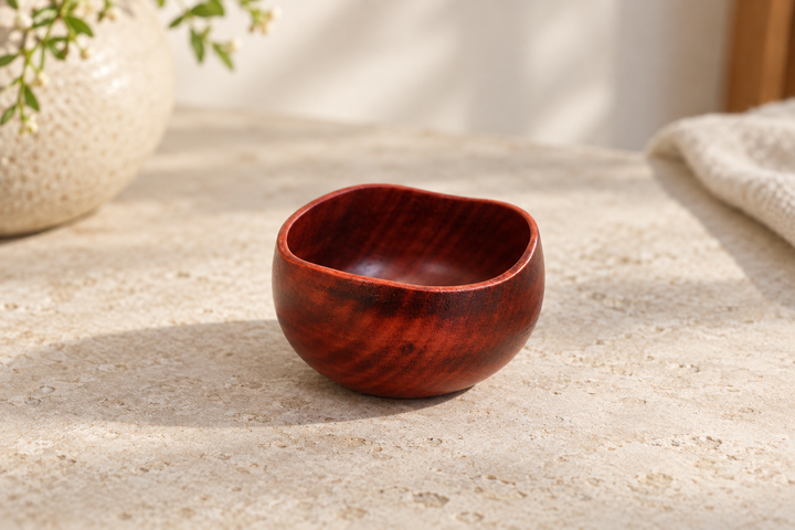 Bud: Berry on a pale stone surface, showing its rounded body, irregular rim, and red-brown wood grain.