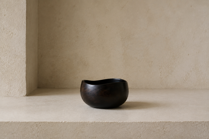 A single small sesame-black lacquerware vessel centered on a dry limestone shelf with generous quiet space.