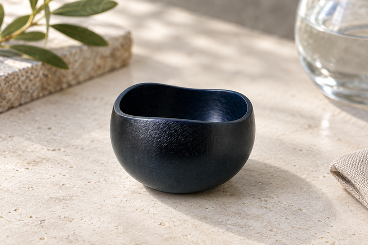 A close view of the empty dark Hyacinth vessel on pale stone, showing its opening and textured lacquer surface.