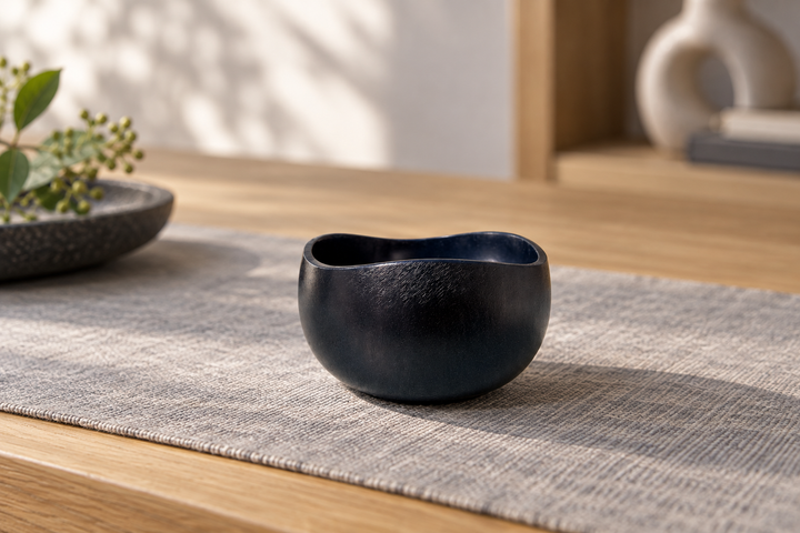 The dark Hyacinth lacquer vessel on a gray woven cloth, with a bowl, books, and a vase in the background.