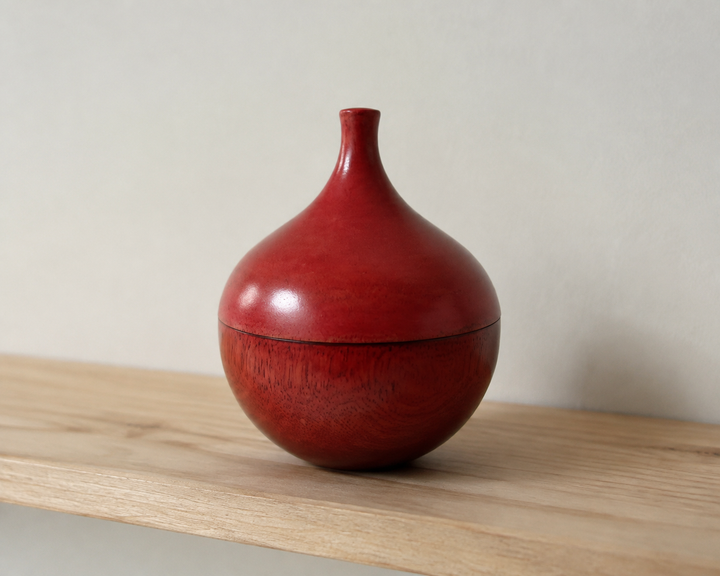A three-quarter view of the closed berry-red Bulb lacquerware object on an eye-level shelf.