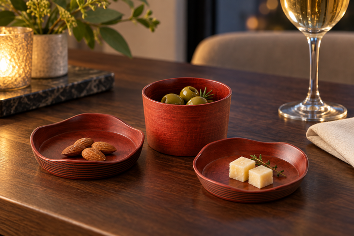 The Berry lacquerware pieces arranged with olives, almonds, and cheese beside a wine glass on a dark table.
